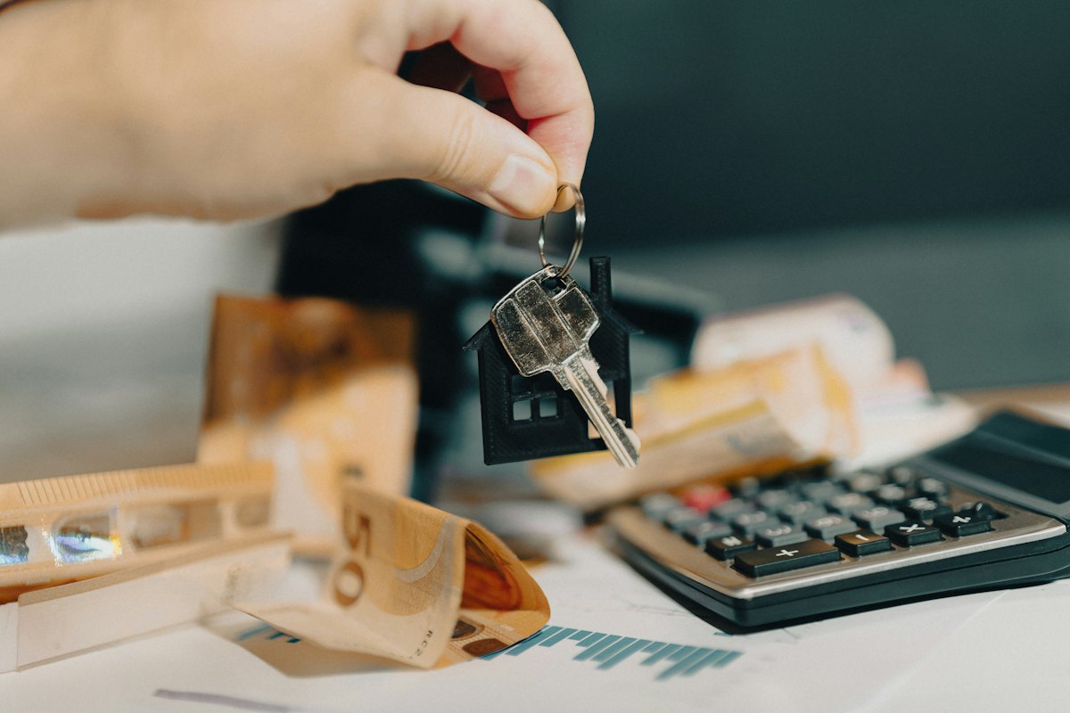 A hand holding a house key in front of a calculator and paperwork