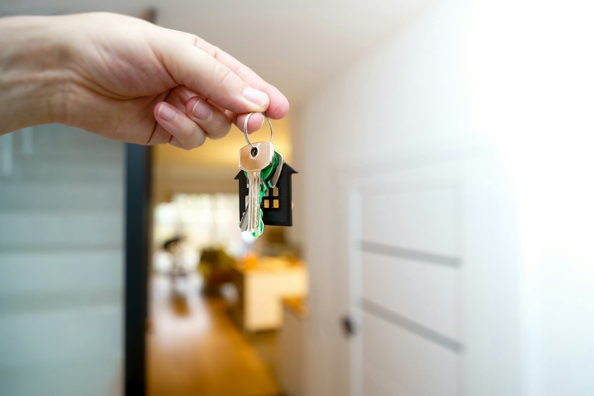Hand holding house keys in front of a front entrance